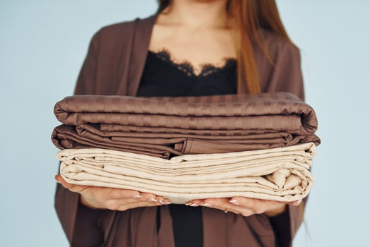 Close up view of young woman that standing against wall with bed clothes in hands photo