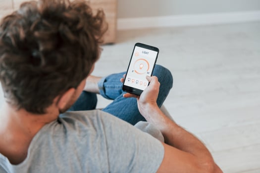 Holds phone. Rear view of adult man that is indoors controlling smart home technology photo