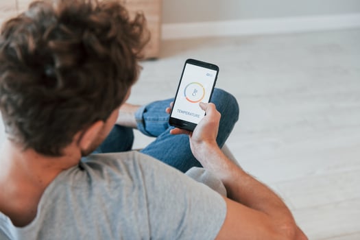 Sits and holds phone in hands. Rear view of adult man that is indoors controlling smart home technology photo