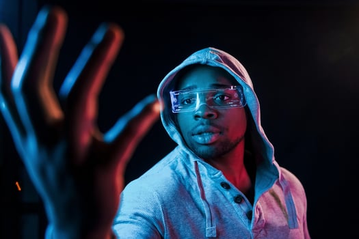 In special eyewear. Futuristic neon lighting. Young african american man in the studio photo