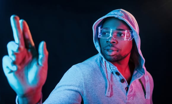 In special eyewear. Futuristic neon lighting. Young african american man in the studio photo