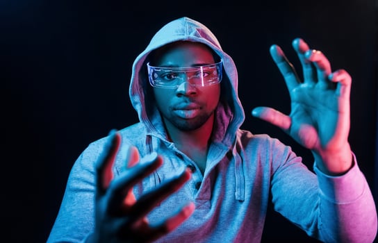 In special eyewear. Futuristic neon lighting. Young african american man in the studio photo