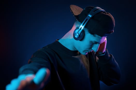Guy uses headphones. Neon lighting. Young european man is in the dark studio photo