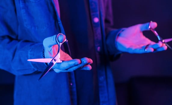 Close up view of barber's hands that holding scissors. Neon lighting photo