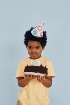 Happy little african american kid have fun indoors at birthday party holds cake photo