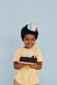 Happy little african american kid have fun indoors at birthday party holds cake photo
