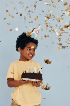 Happy little african american kid have fun indoors at birthday party holds cake photo