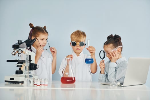 Standing by the table with test tubes. Children in white coats plays a scientists in lab by using equipment photo