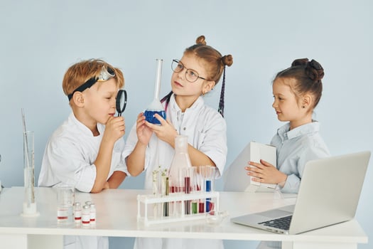 Standing by the table with test tubes. Children in white coats plays a scientists in lab by using equipment photo