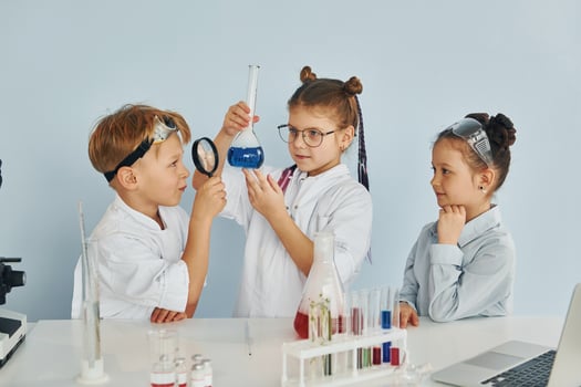 Standing by the table with test tubes. Children in white coats plays a scientists in lab by using equipment photo
