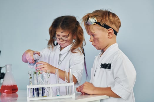 Little girl and boy in white coats plays a scientists in lab by using equipment photo