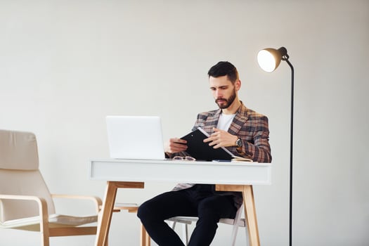 Uses laptop. Young stylish businessman in suit indoors. Conception of success photo
