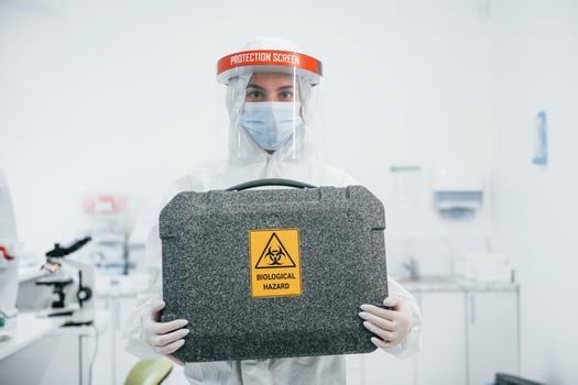 Holds case with biological hazard. Female medical worker in protective uniform works on COVID-19 vaccine photo