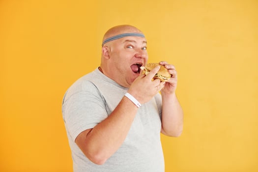 With fast food. Funny overweight man in sportive head tie is against yellow background photo