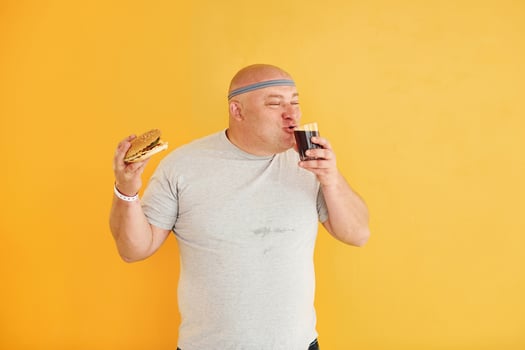 With fast food. Funny overweight man in sportive head tie is against yellow background photo