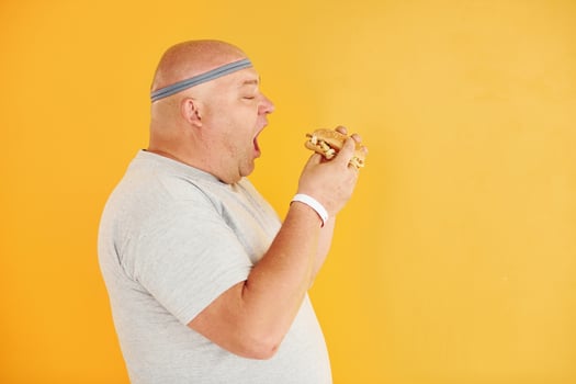 With fast food. Funny overweight man in sportive head tie is against yellow background photo