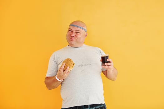 With fast food. Funny overweight man in sportive head tie is against yellow background photo