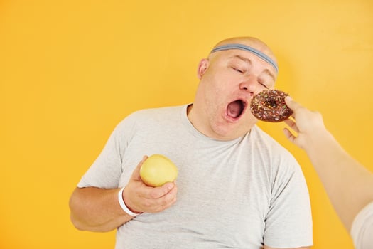 Apple or cookie. Funny overweight man in sportive head tie is against yellow background photo