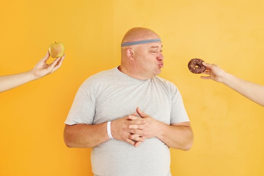 Apple or cookie. Funny overweight man in sportive head tie is against yellow background photo