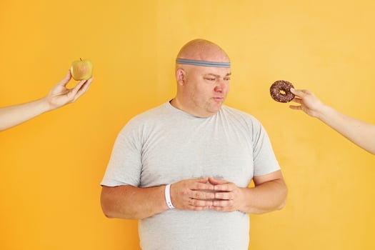 Apple or cookie. Funny overweight man in sportive head tie is against yellow background photo