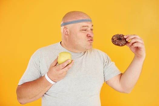 Apple or cookie. Funny overweight man in sportive head tie is against yellow background photo