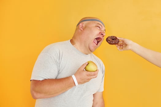 Apple or cookie. Funny overweight man in sportive head tie is against yellow background photo