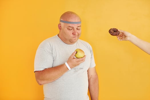Apple or cookie. Funny overweight man in sportive head tie is against yellow background photo