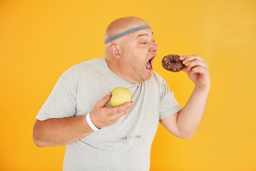 Apple or cookie. Funny overweight man in sportive head tie is against yellow background photo