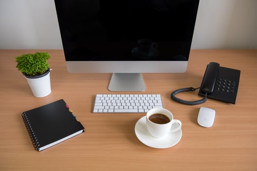 Office table with personal computer, note book, phone, keyboard, mouse, coffee cup and plant pot photo