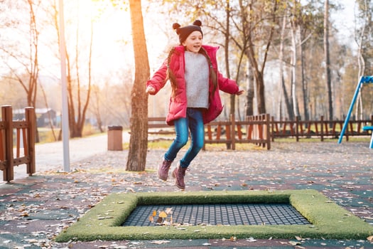 Happy school girl jumping on a small trampoline in the park photo