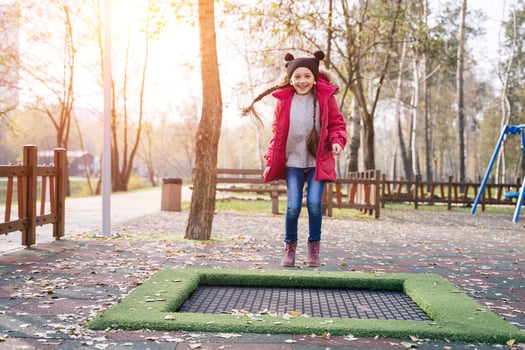 Happy school girl jumping on a small trampoline in the park photo