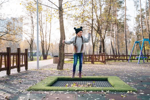Happy school girl jumping on a small trampoline in the park photo