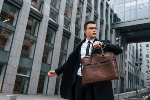 Grey building behind. Businessman in black suit and tie is outdoors in the city photo
