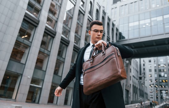 Grey building behind. Businessman in black suit and tie is outdoors in the city photo