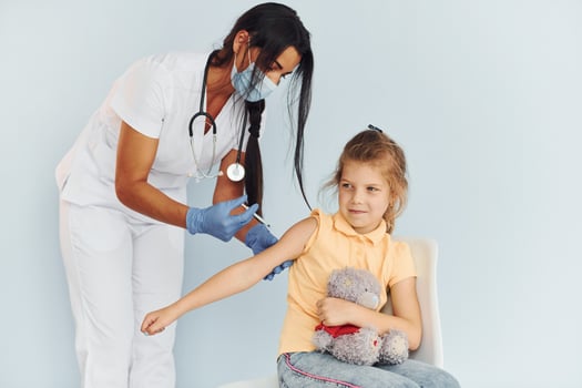 Little girl with teddy bear. Doctor in uniform making vaccination to the patient photo