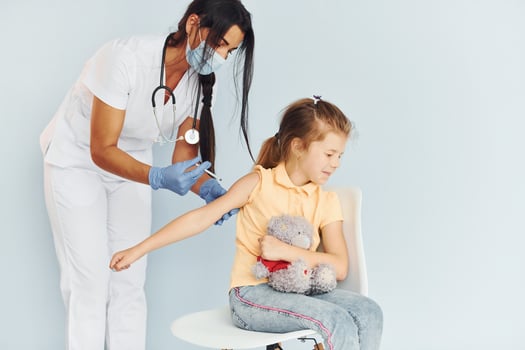 Little girl with teddy bear. Doctor in uniform making vaccination to the patient photo