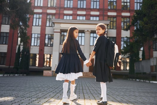 Rear view. Two schoolgirls is outside together near school building photo