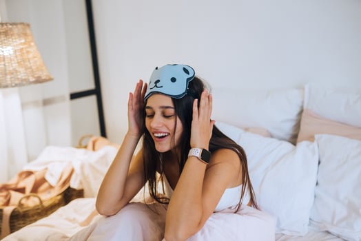 Sleepy woman waking up while sitting in bed on white background photo