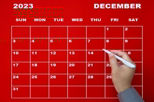 December 2023 calendar with hand holding black pen on red background. photo