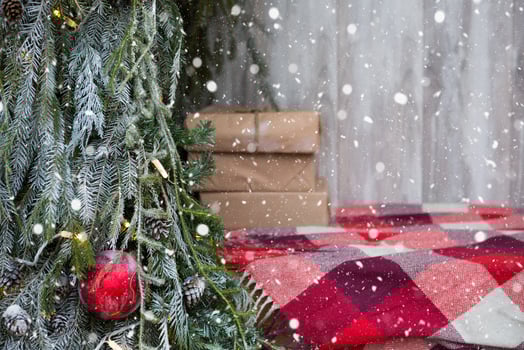 Boxes with gifts for Christmas in kraft paper lie on a red plaid plaid near the outdoor Christmas tree. Street decorations of the city, snow, New Year mood, fairy lights photo