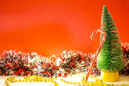 Christmas tree on a red background with lights of garlands, caramel striped cane, Santa hat, tinsel. New year, festive atmosphere. Copy space photo