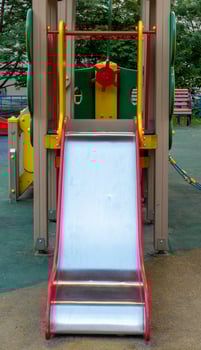 An element of a children's swing. slide. An outdoor colorful playground next to the house. A summer day. Children's playground with rubber floor covering. photo