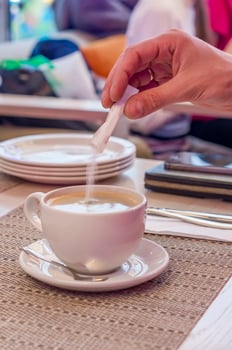 A Hand adding sugar to a cup of black coffee photo