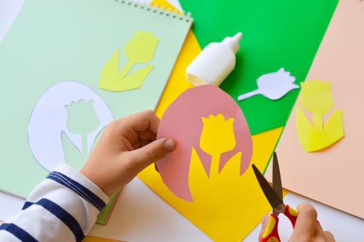 A small child makes paper crafts for mother's day or birthday. A boy makes paper flowers for mom. A simple pleasant idea of a children's gift to mom. photo