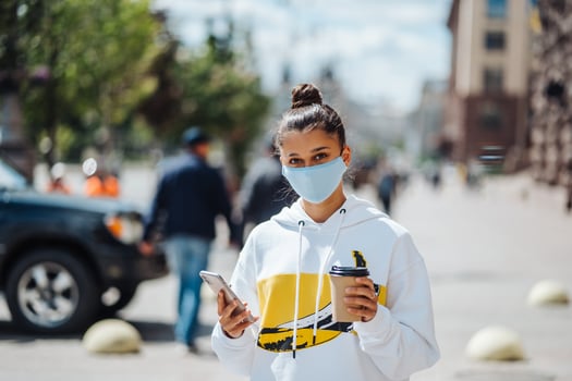 Young woman holding coffee wearing protective medical mask photo