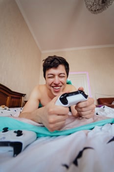 Guy lying in bed and playing video game, holding controller photo