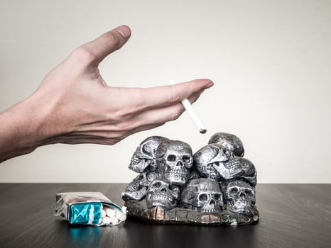 Male hand holding cigarette, skulls on the table, Anti smoking concept photo