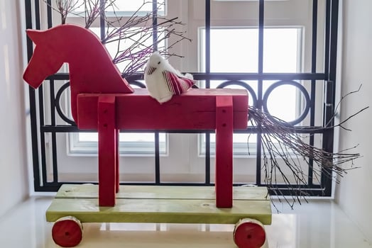 Red wooden horse and knitted bird standing on window sill as interior decoration photo