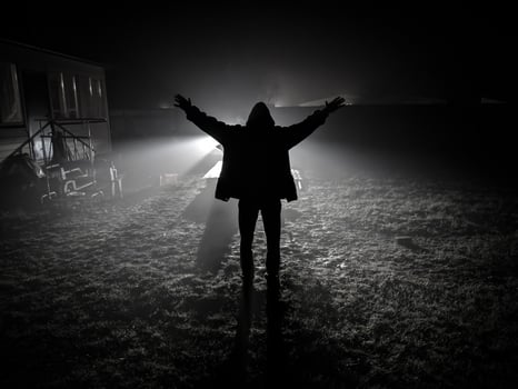 silhouette of man from back side with hands up outdoors against car lights photo