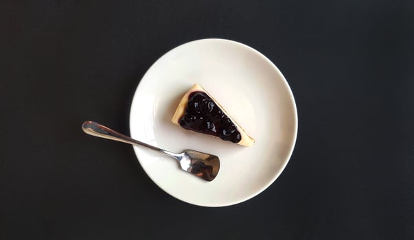 Top view of slice of blueberry cheesecake and stainless steel spoon in white dish or plate on black background with copy space. Flat lay of sweet dessert and Homemade food on dark table photo